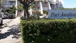 Et skilt med teksten 'Port Jonathan' foran en bygning med altaner og et træ.