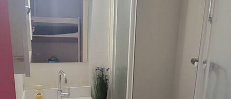 A compact bathroom with a sink, mirror, shower, and a small white appliance.
