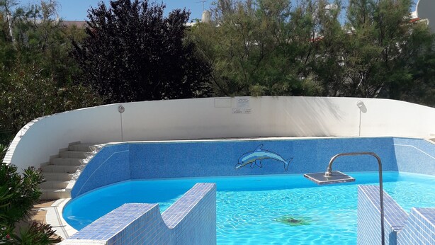 En swimmingpool med flisekant, en livredderstand og et skilt der angiver sauna og pool.