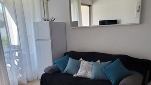 En moderne stue med en sort sofa, et lille bord og et stort vindue med gardiner.