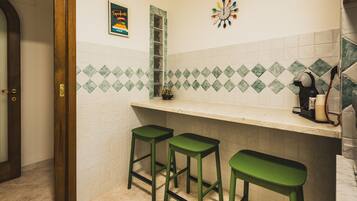 A kitchen with a white countertop, green stools, a clock, and a coffee maker.