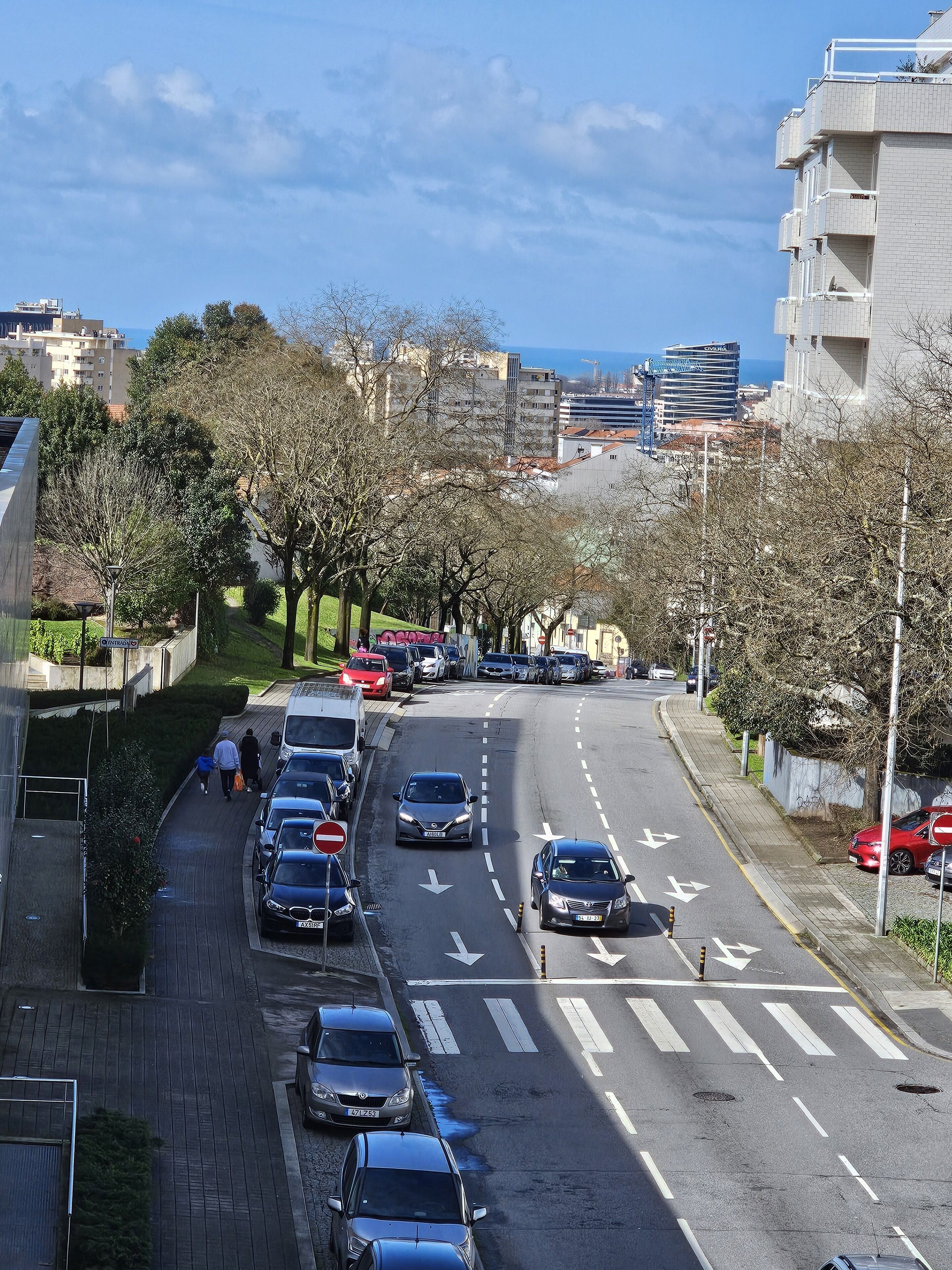 Een stadsstraat met geparkeerde auto's, een zebrapad en gebouwen op de achtergrond.