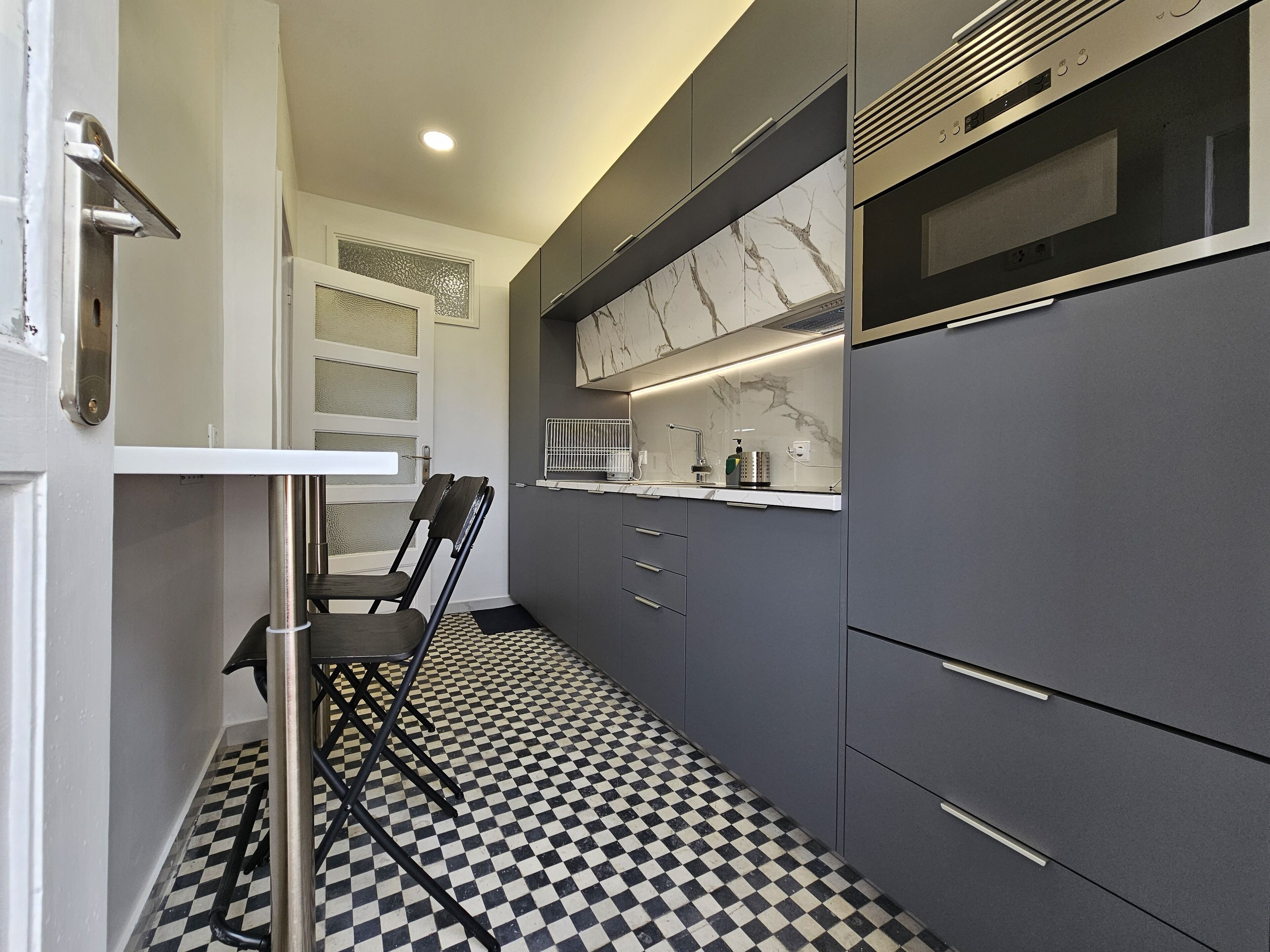 Una cucina moderna con pavimento a scacchi, un forno a microonde integrato e una sedia vicino alla porta.