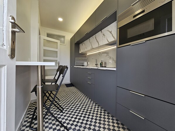 A modern kitchen with a checkered floor, a built-in microwave, and a chair near the door. - LM Art Apartments (Porto)