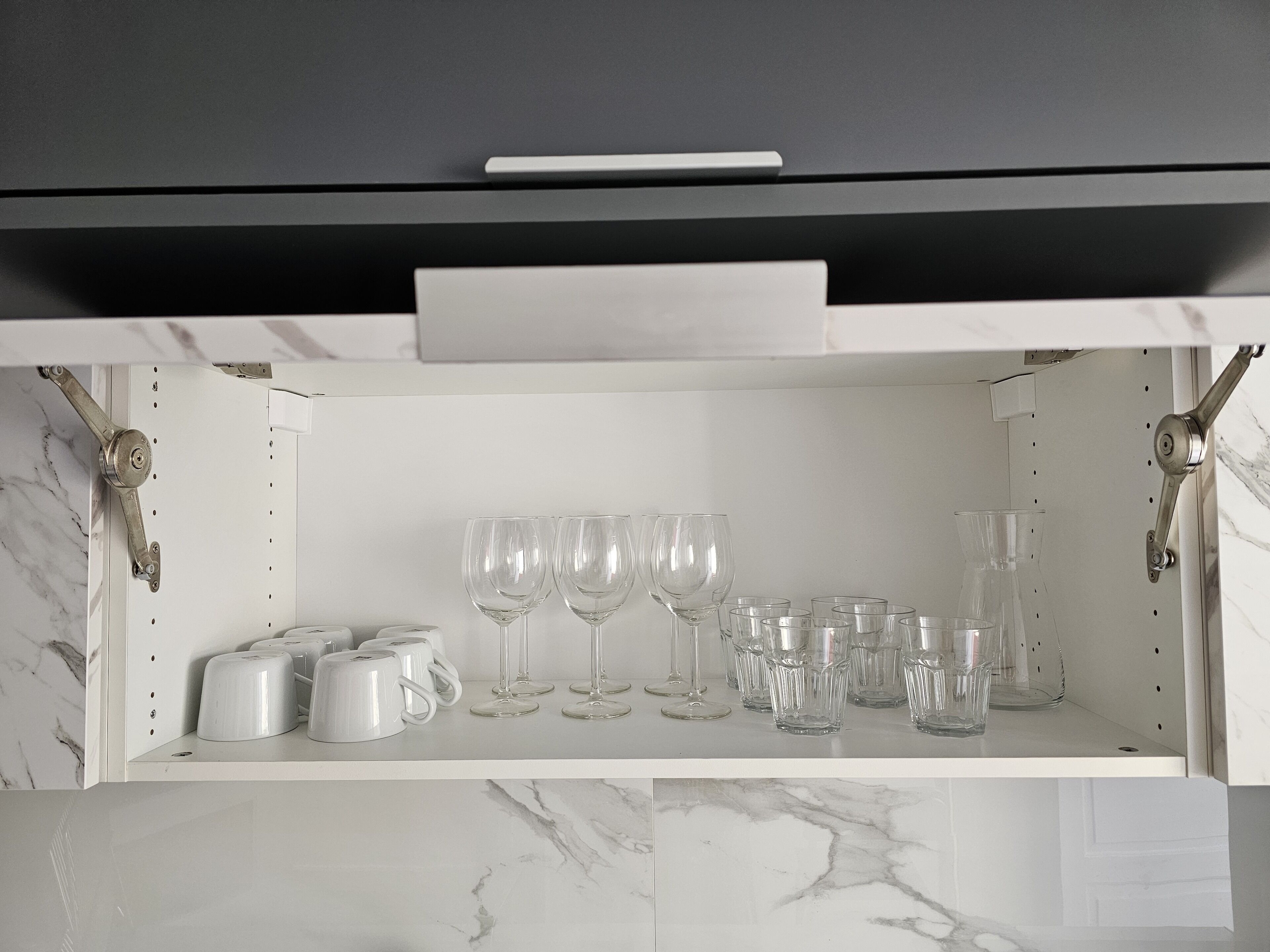 Eine Küche mit Marmorarbeitsplatte, einem weißen Schrank mit Schublade sowie verschiedenen Gläsern und Tassen.