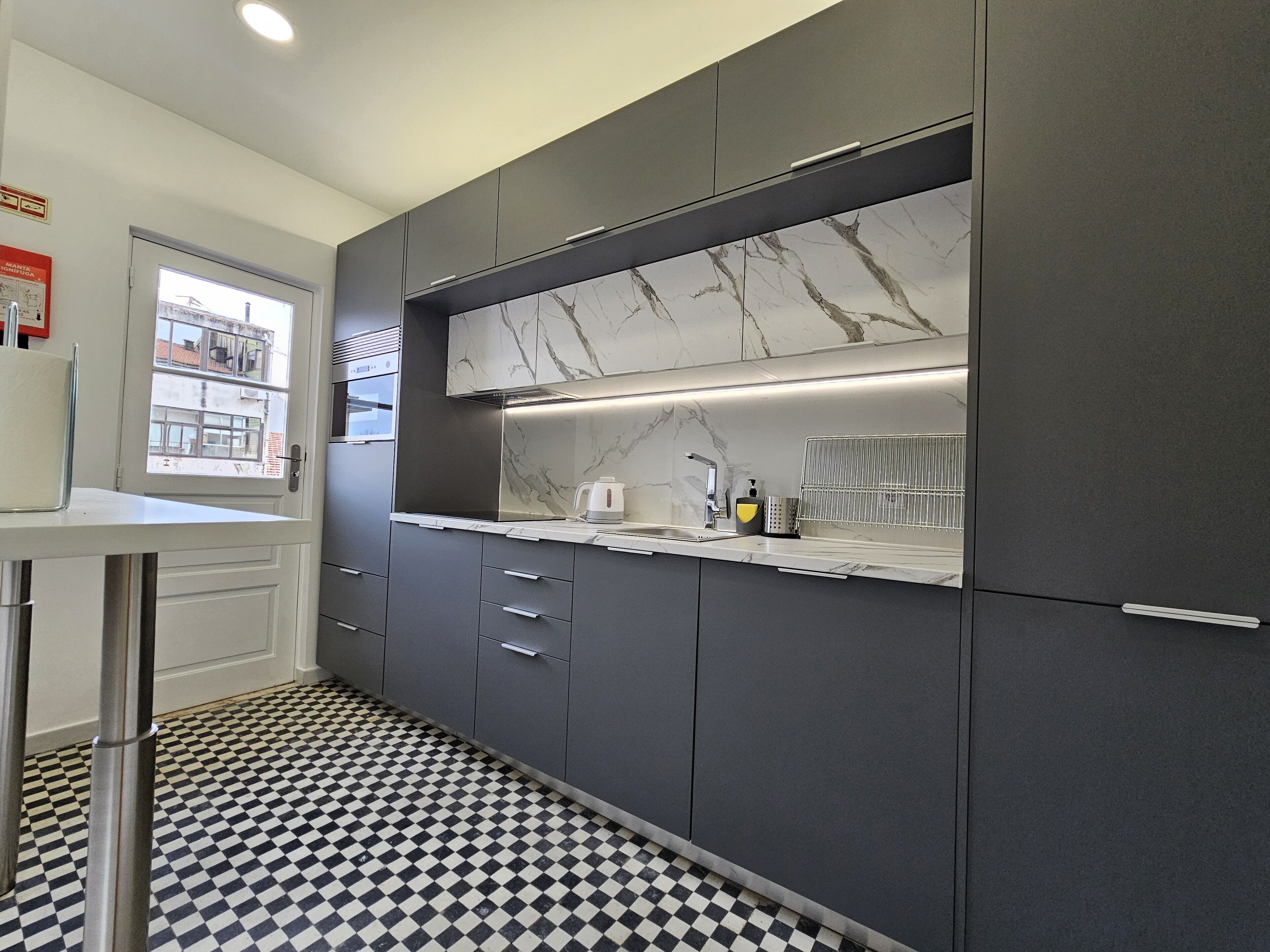 A modern kitchen with grey cabinets, a marble backsplash, and a checkered floor.