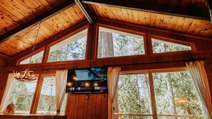 Une cabane avec un intérieur en bois, de grandes fenêtres et une cheminée.