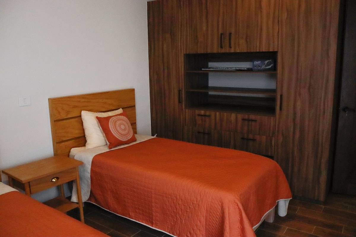 A bedroom with two beds, a wooden wardrobe, and a built-in TV shelf.