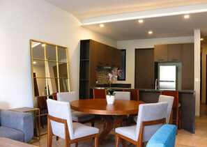 Un comedor moderno con una mesa redonda de madera, seis sillas grises tapizadas y un jarrón decorativo con flores.