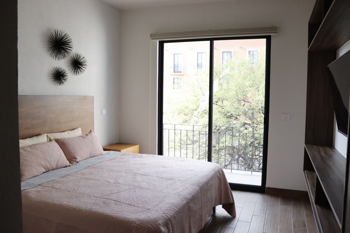 A bedroom with a large bed, a nightstand, a wall-mounted light fixture, and a sliding glass door leading to a balcony.
