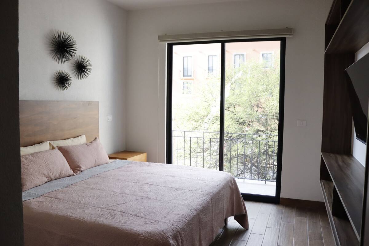 Ein Schlafzimmer mit einem großen Bett, einem Nachttisch, einer Wandleuchte und einer Schiebeglastür, die auf einen Balkon führt.
