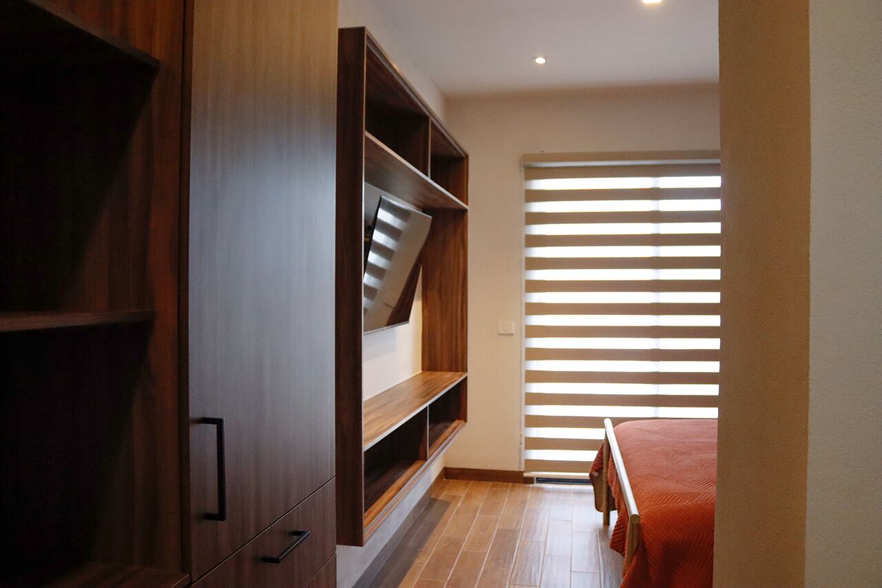 A bedroom with a wooden wardrobe, a bed with a red blanket, and a window with horizontal blinds.