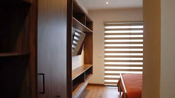 A bedroom with a wooden wardrobe, a bed with a red blanket, and a window with horizontal blinds.