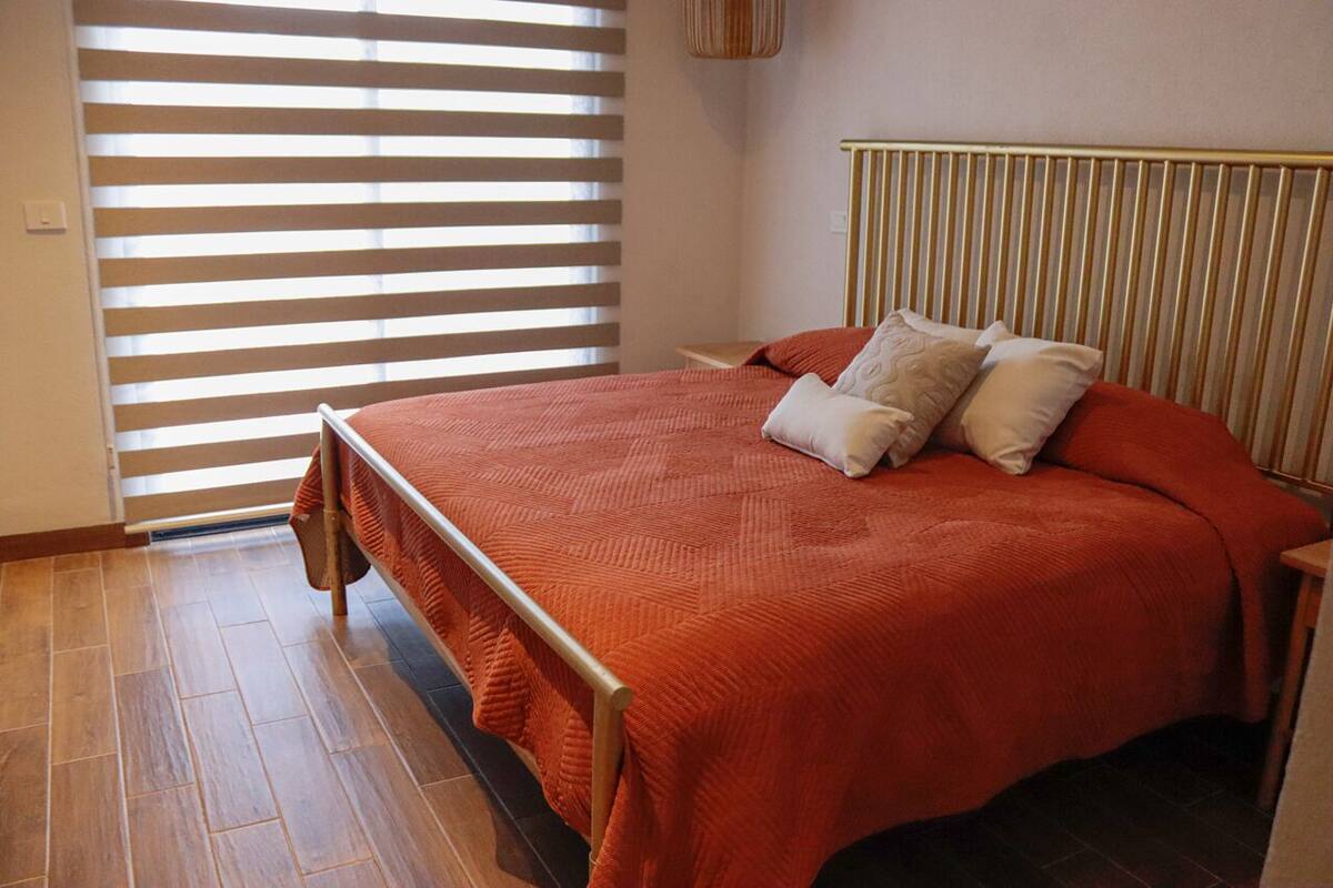 Ein Schlafzimmer mit einem Bett, Holzboden und einem Fenster mit Jalousien.