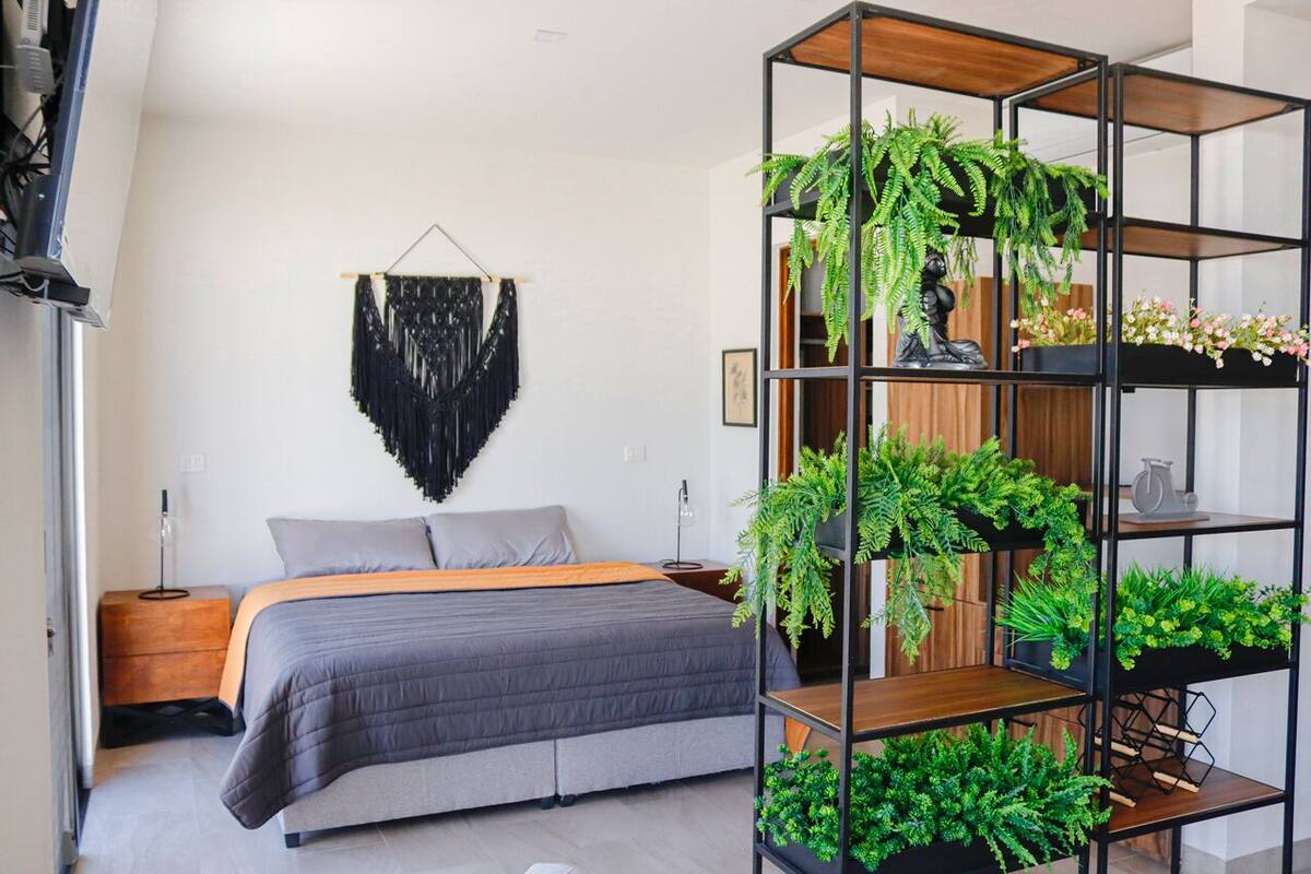 Ein modernes Schlafzimmer mit einem Bett, einer Wanddekoration aus Makramee und einem Regal mit Pflanzen.