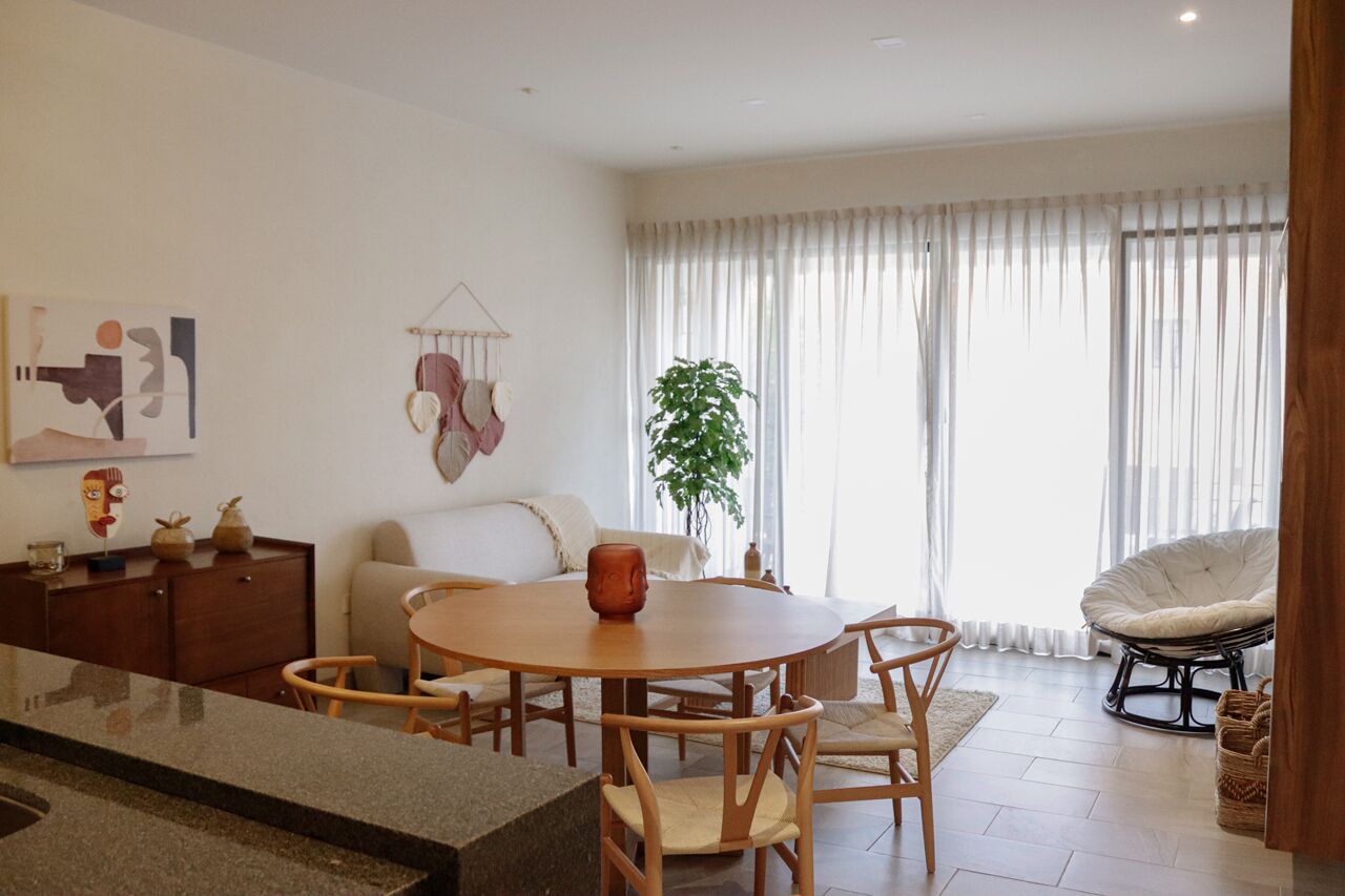 Un salon moderne avec une table ronde en bois, un canapé, un fauteuil et une plante en pot.