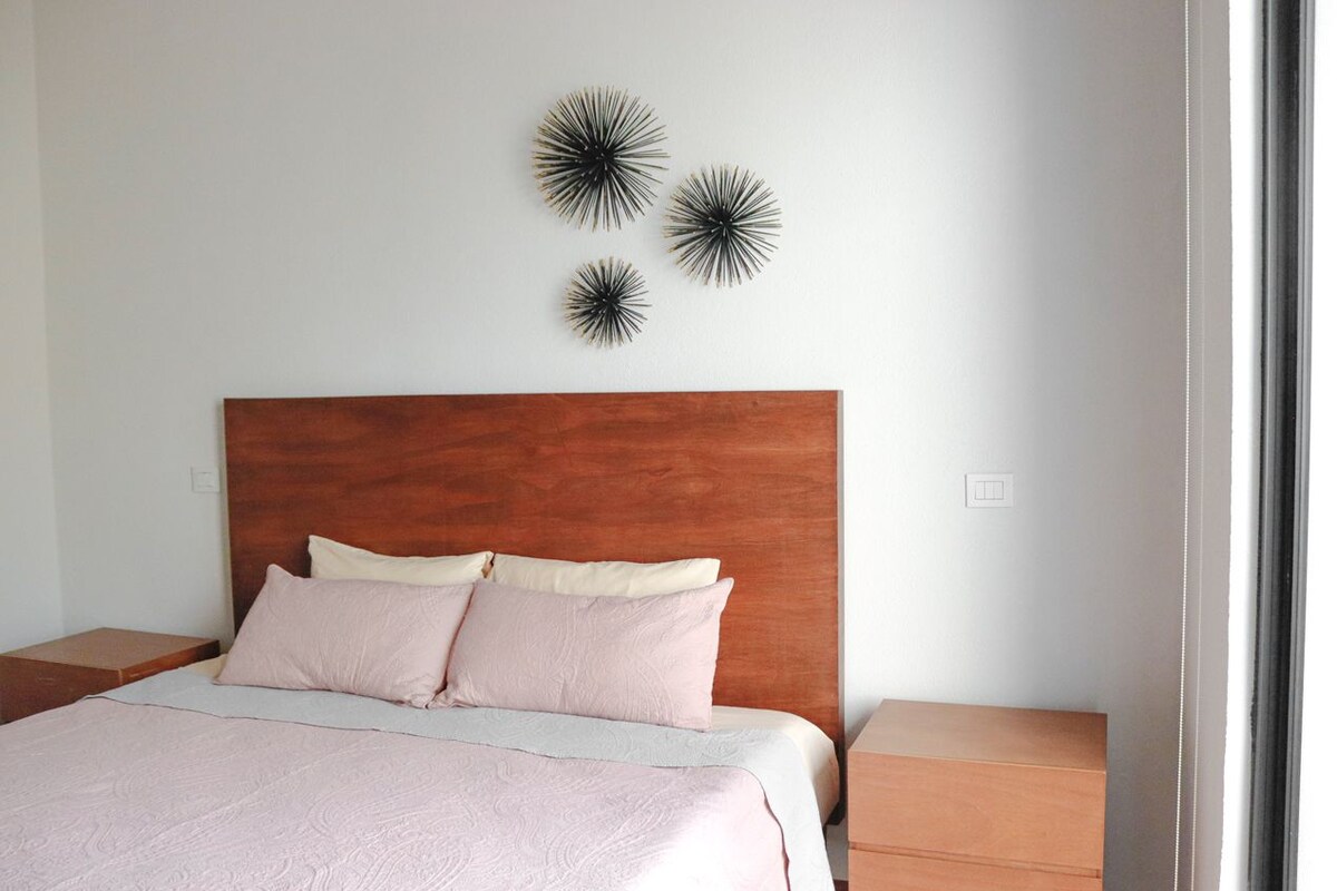 Una cama bien hecha con cabecera de madera, dos mesitas de noche y decoración en la pared.