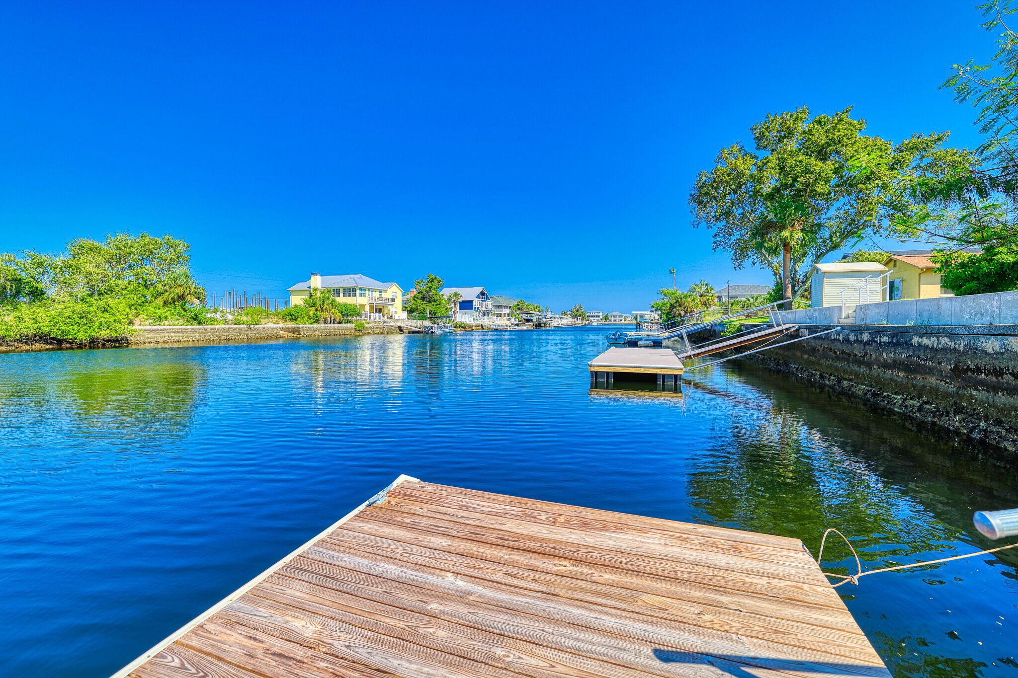A wooden dock extending into calm water with a clear blue sky above.