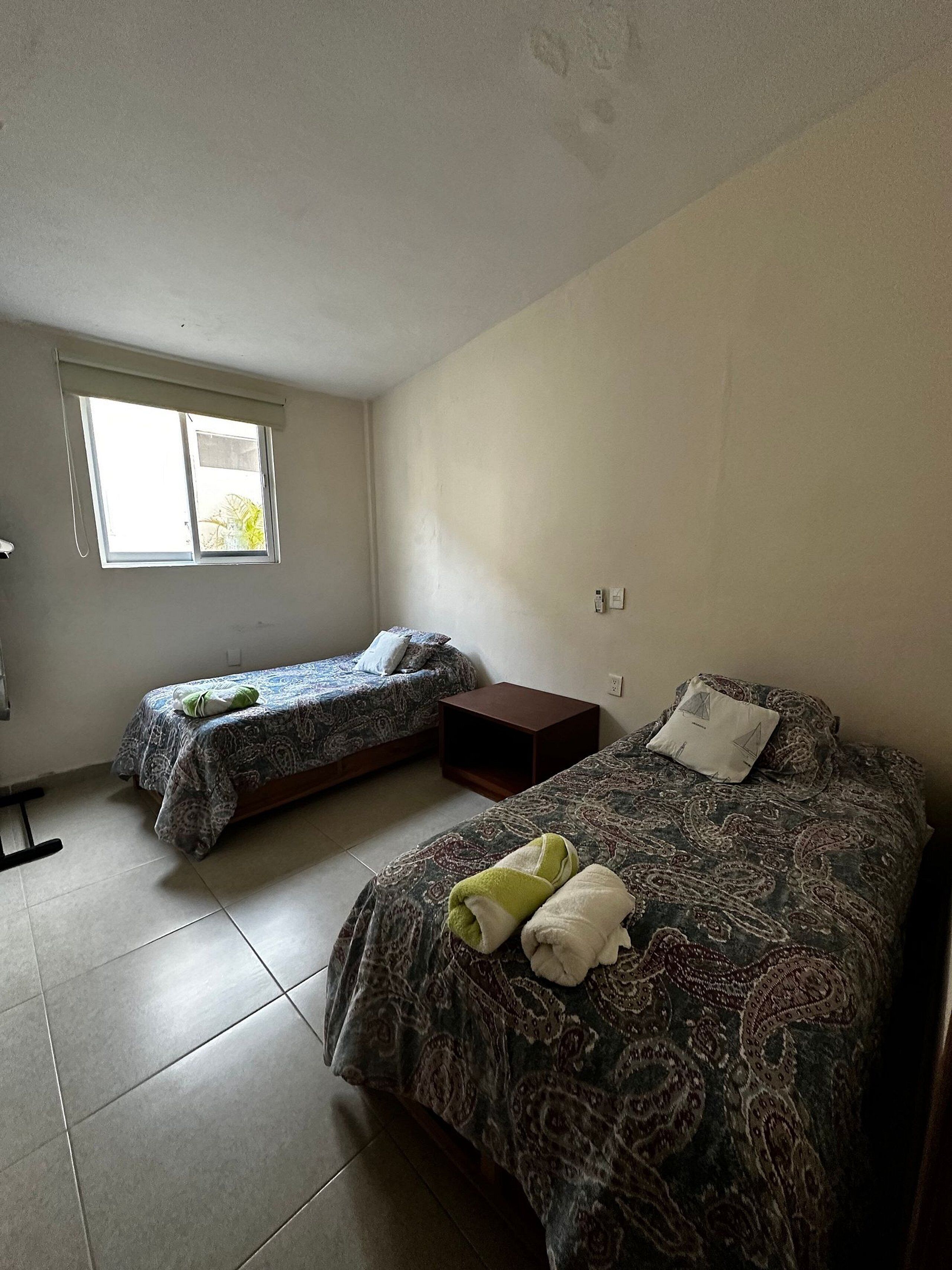Un dormitorio con dos camas individuales, una ventana y piso de baldosas.