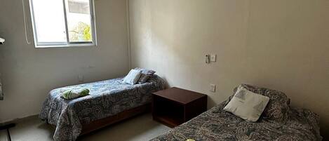 Un dormitorio con dos camas individuales, una ventana y piso de baldosas.