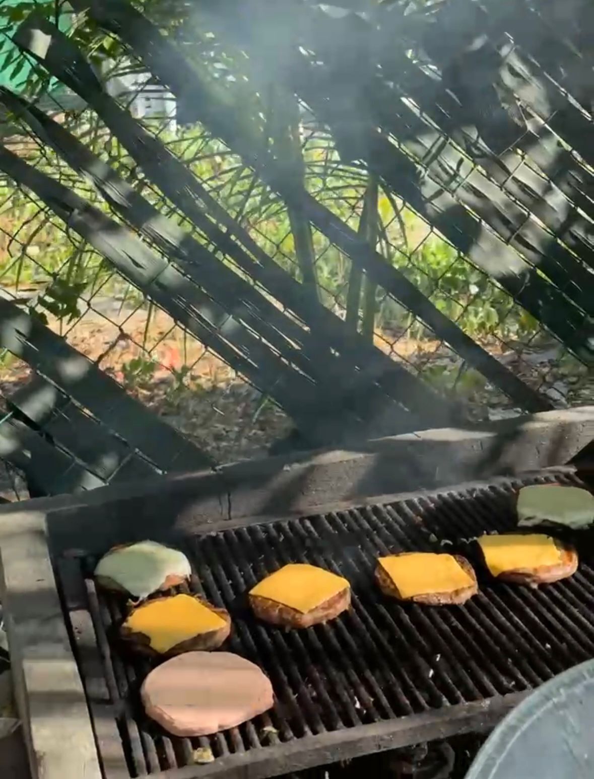 A grill with several burgers and cheese patties being cooked outdoors.
