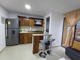 Una cocina compacta con armarios de madera, un refrigerador, un lavamanos y un pequeño comedor con taburetes.