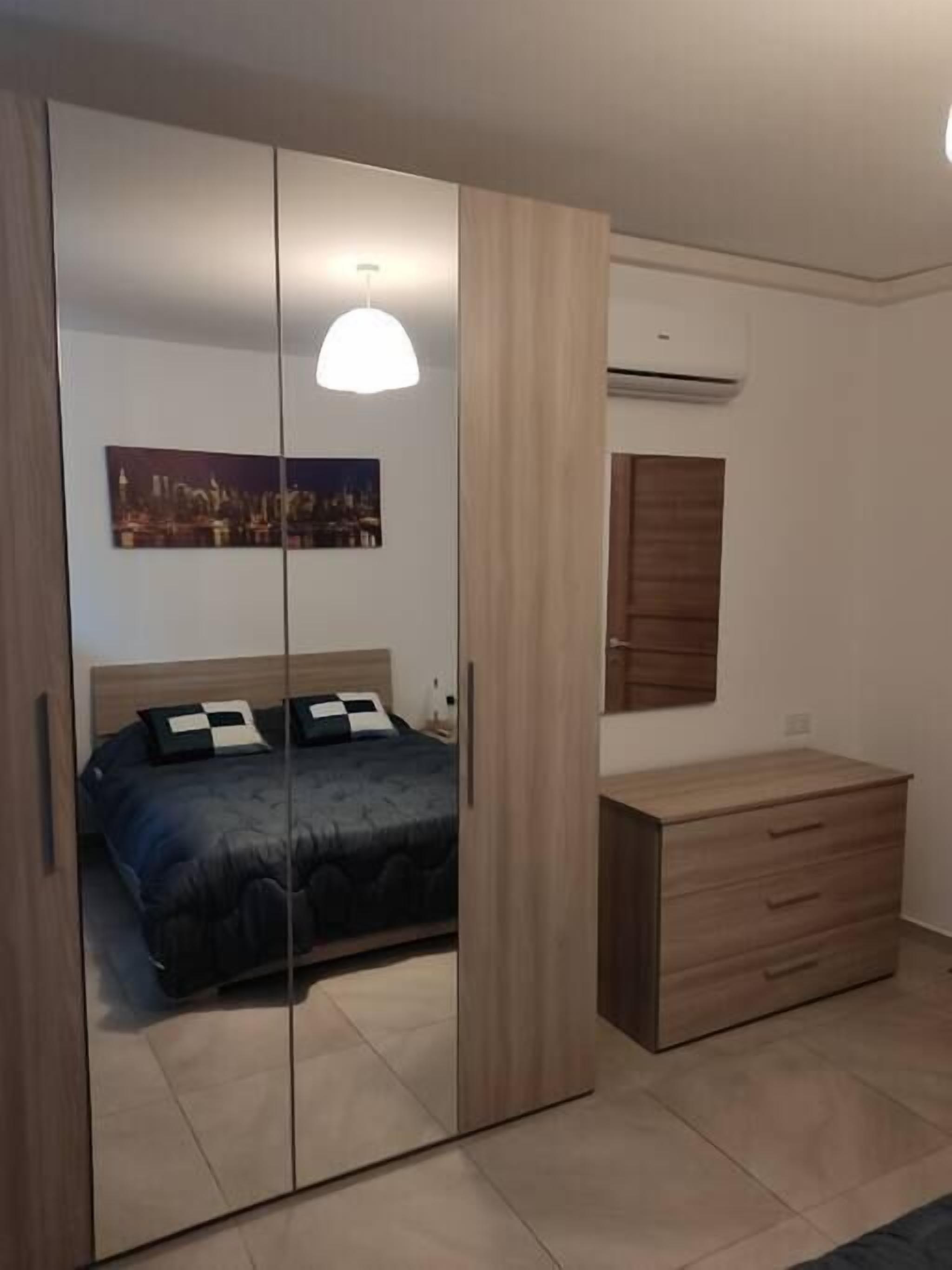 A bedroom with a bed, a wardrobe, a dresser, and a painting on the wall.