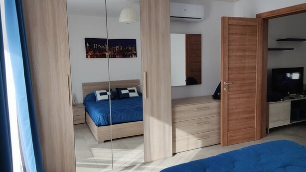 Et moderne soveværelse med seng, fjernsyn og garderobe.
