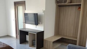 Uma sala de estar moderna com um sofá cinzento, uma televisão fixada na parede, um móvel de entretenimento em madeira e uma porta que dá para outro cômodo.
