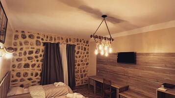 Habitación de hotel con pared de piedra, banco de madera, televisión y cama con toallas.