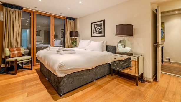 Habitación de hotel moderna con una cama grande, una mesita de vidrio, una silla y vistas a la ciudad a través del ventanal.