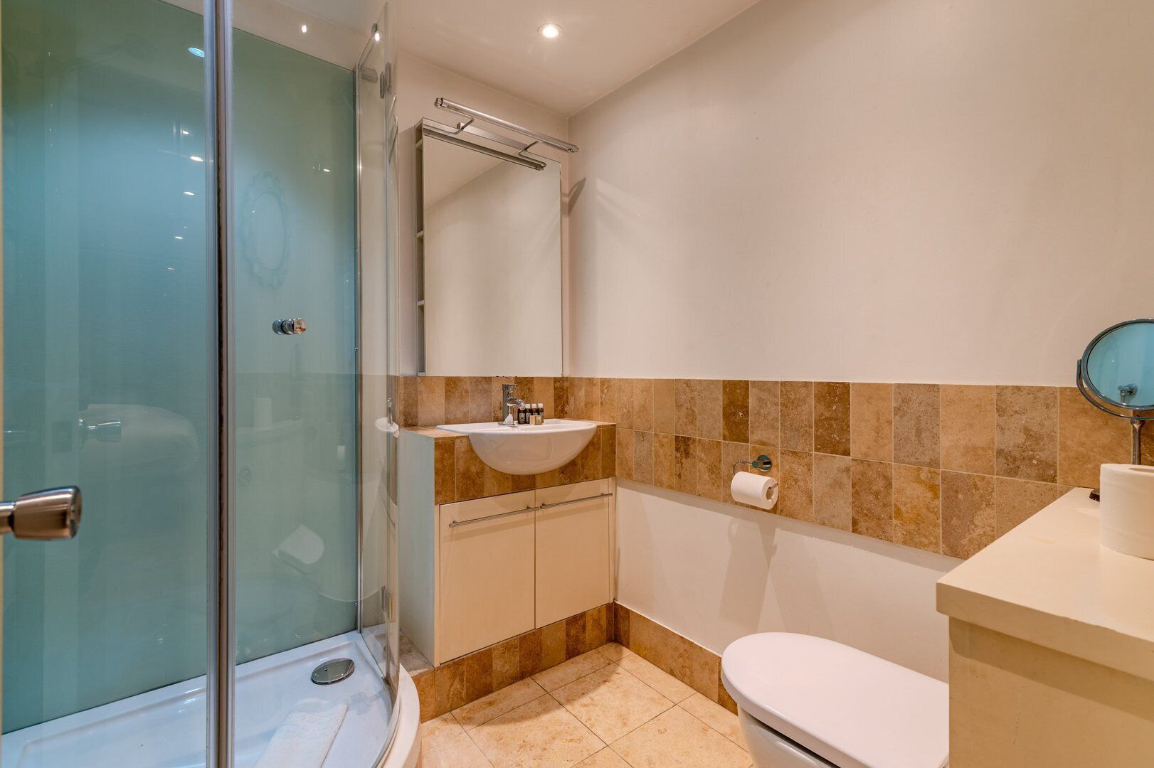 Um banheiro moderno com box de vidro, pia com bancada de mármore e vaso sanitário.
