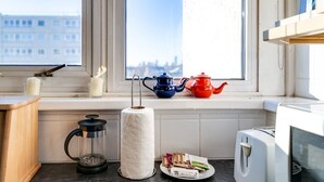 A kitchen with a window, a stove, a kettle, a teapot, a candle, and a plate with tea bags. - Cosy Battersea Flat (London)