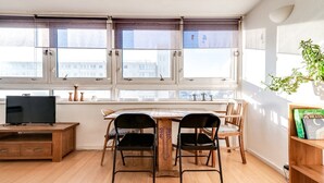 A dining area with a wooden table, two chairs, a TV on a wooden stand, and a bookshelf with books. - Cosy Battersea Flat (London)