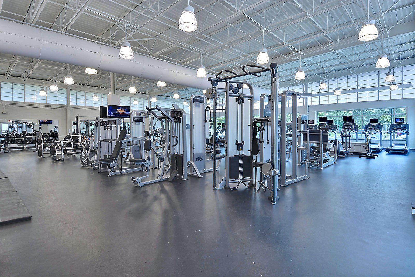 Een sportschool met diverse trainingsapparaten, grote ramen en een hoge plafond.