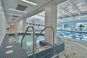 Una piscina techada con carriles delimitados, una silla de salvavidas y piso de baldosas.