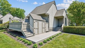 Una casa moderna de dos pisos con fachada gris, una terraza de madera y un pequeño porche delantero.