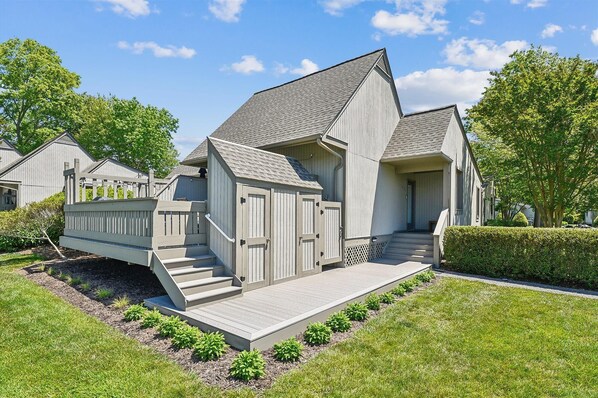 A modern two-story house with a grey exterior, a wooden deck, and a small front porch. - Lakefront Sea Colony Villa! Amenity Rich with Private Beach and Shuttle! (Bethany Beach)