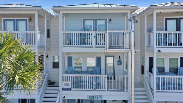 A beachfront hotel with two-story balconies, a visible sign for 'Pristine Properties', and a palm tree in the foreground. - The Blue Pearl (Port St. Joe)