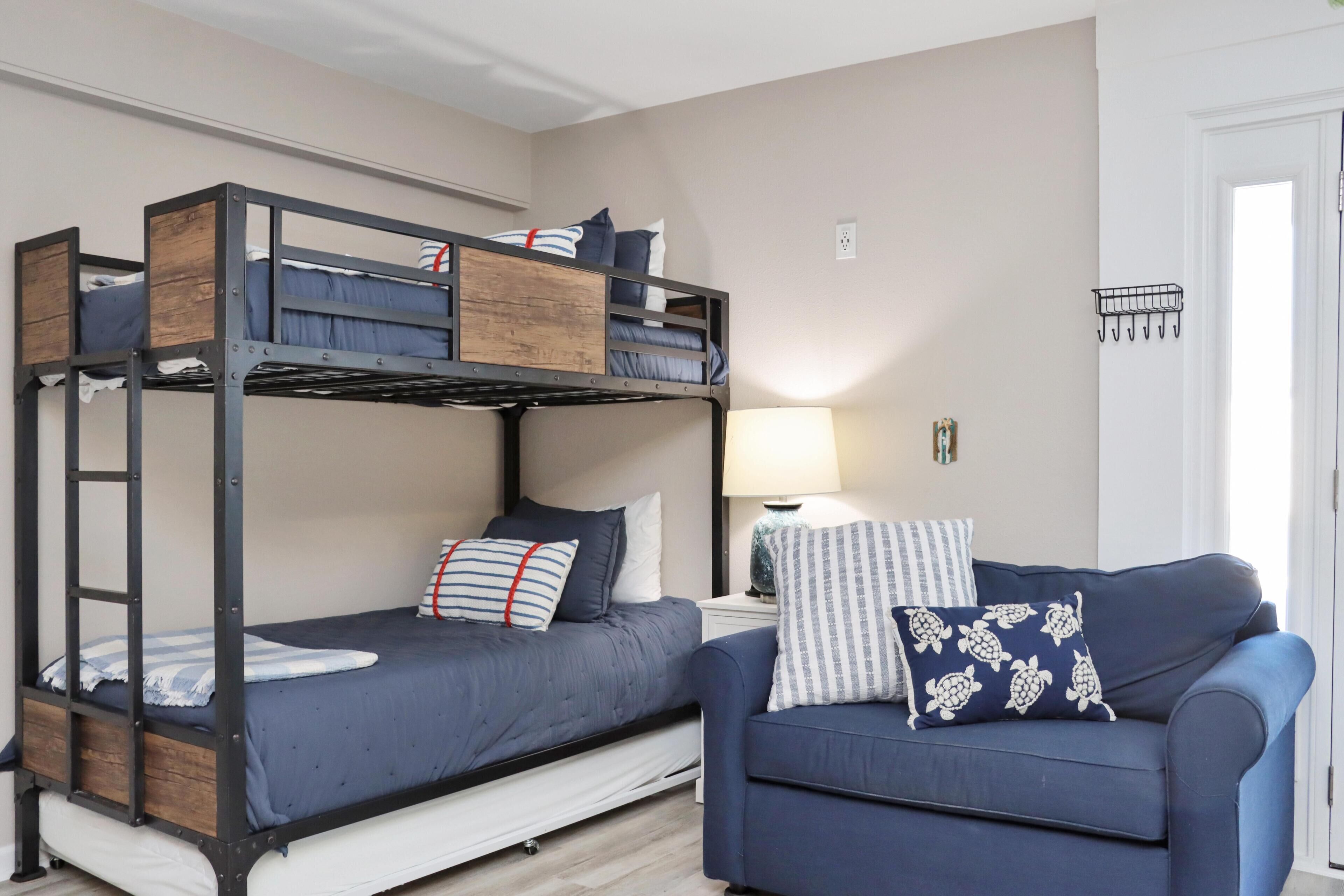 A bunk bed with a desk and chair, a lamp, and a couch with a turtle-patterned pillow.