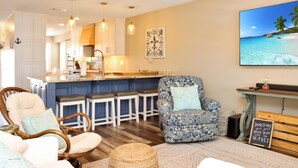 A modern living room with a large TV, a bar area, and a kitchen in the background. - The Blue Pearl (Port St. Joe)