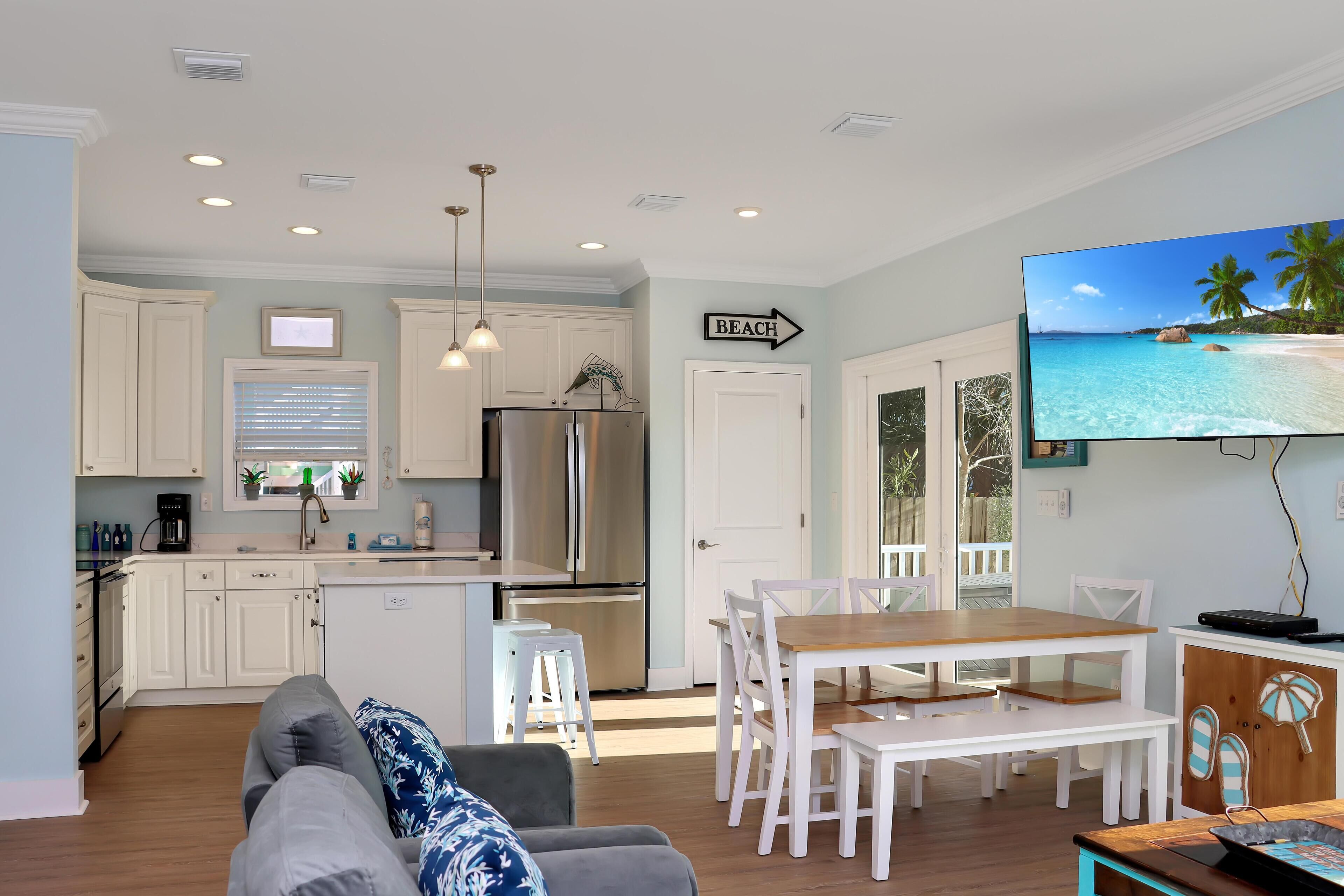 A modern kitchen with white cabinets, a stainless steel refrigerator, and a dining area with white chairs and a wooden table.