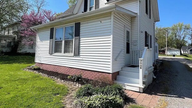 A single-story white house with a brick foundation, a front porch, and a small front yard. - Oak Street Station in Downtown Mahomet (Mahomet)