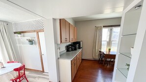 A compact kitchen with wooden cabinets, a dining area with a red chair, and a small table. - Oak Street Station in Downtown Mahomet (Mahomet)