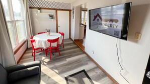 A modern living room with a dining area, a ceiling fan, a flat-screen TV, and a view of the outdoors. - Oak Street Station in Downtown Mahomet (Mahomet)