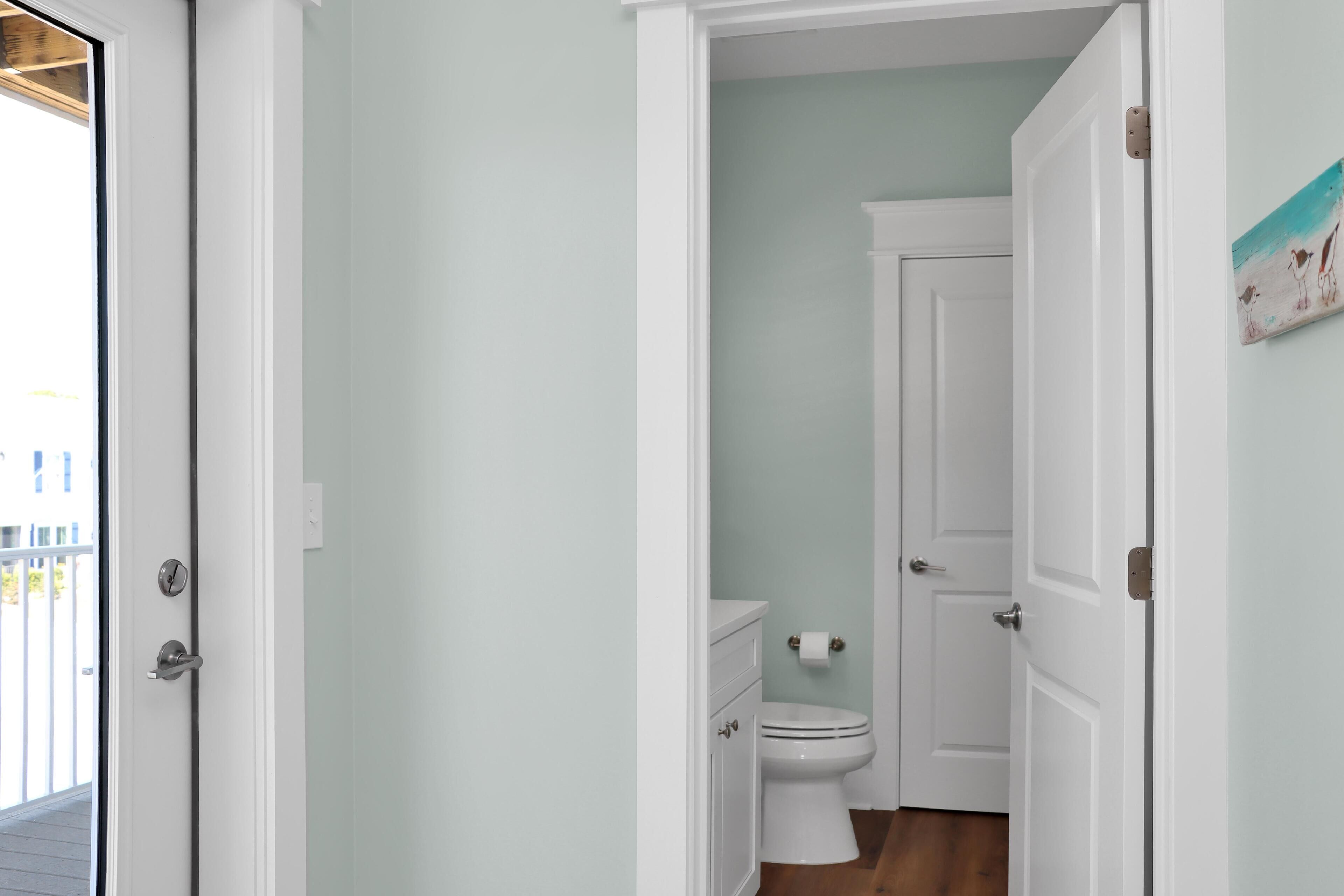 Un pasillo estrecho con una puerta blanca a la izquierda y un inodoro blanco con un rollo de papel higiénico a la derecha.
