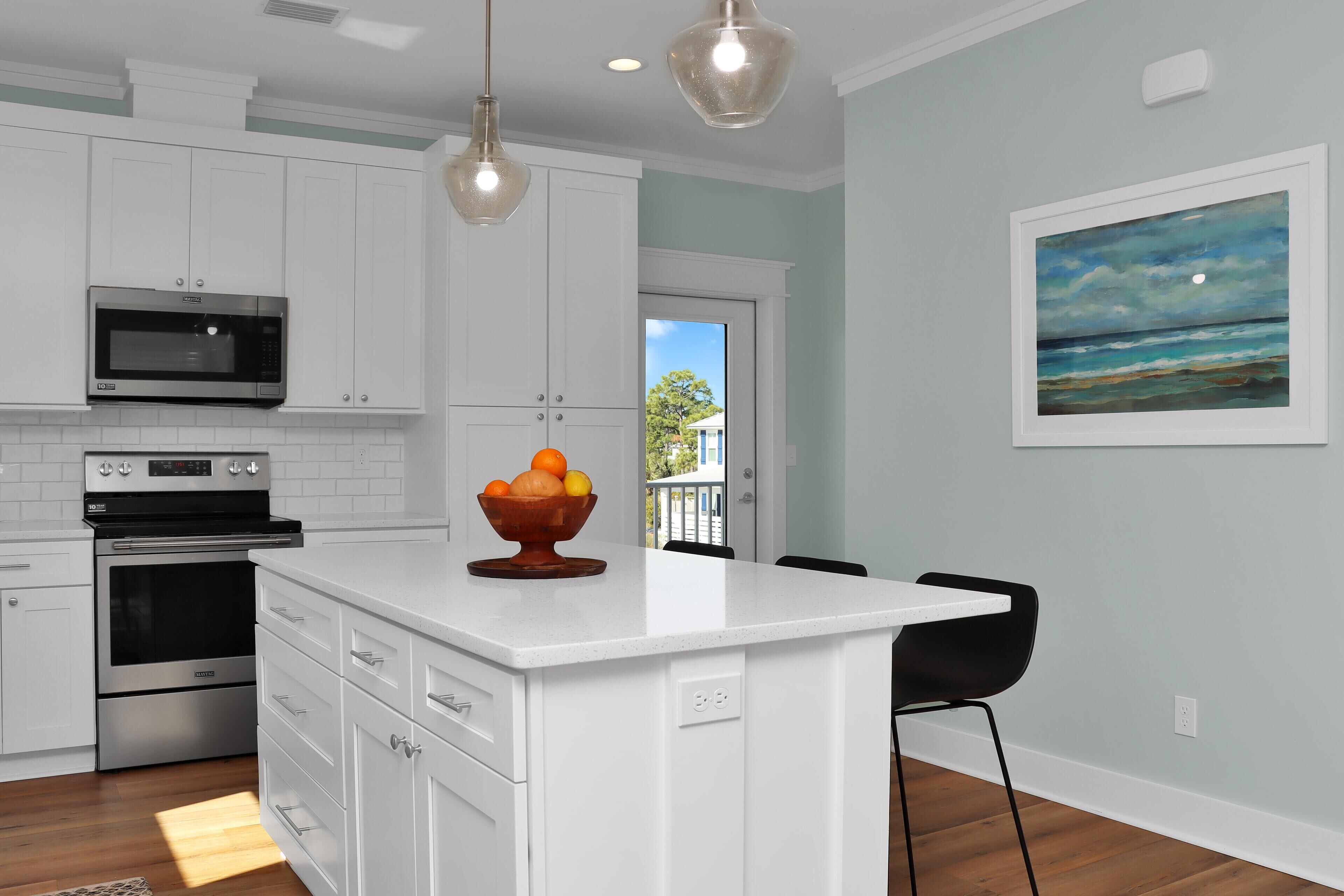 A modern kitchen with white cabinetry, a built-in microwave, and an island with a bowl of fruit.