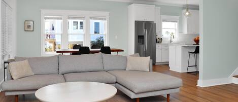 A modern living room with a sectional sofa, a round coffee table, and a kitchen in the background.