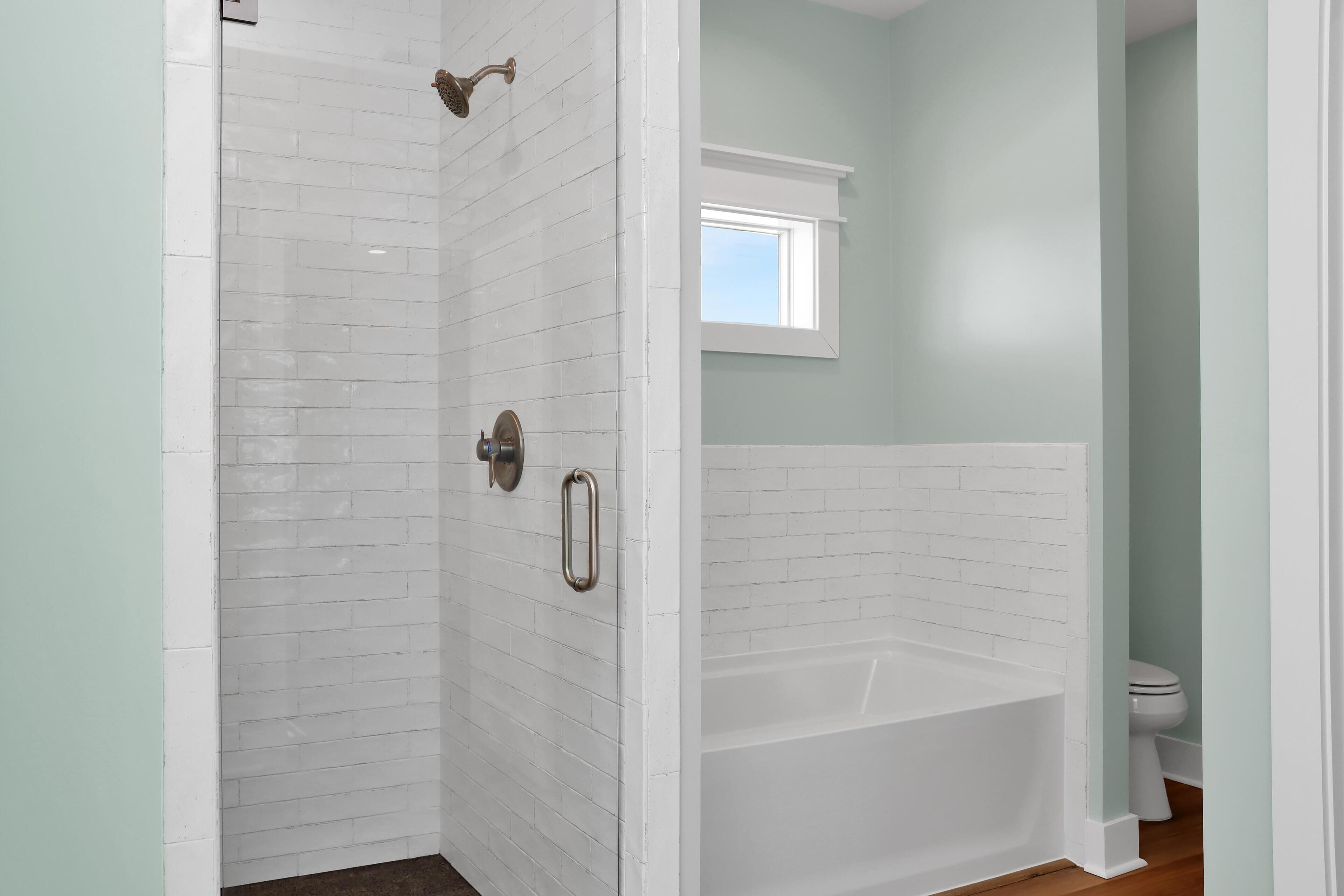 A bathroom with white subway tiles, a bathtub, a toilet, and a window.