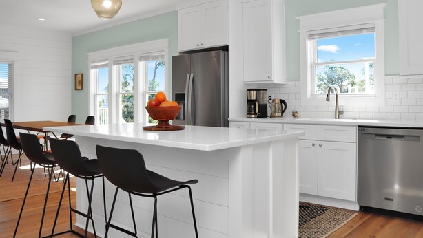 Una cocina moderna con armarios blancos, un refrigerador de acero inoxidable y una isla grande con taburetes de bar.